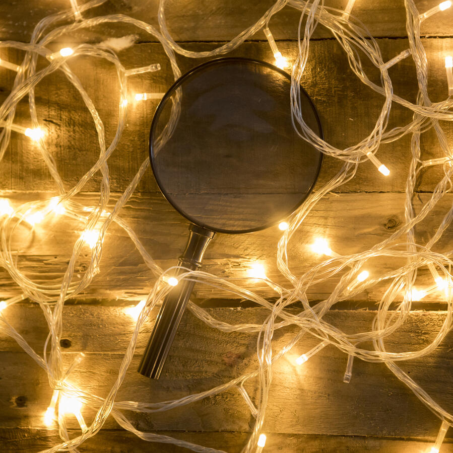 Magnifying glass and Christmas lights on wooden background